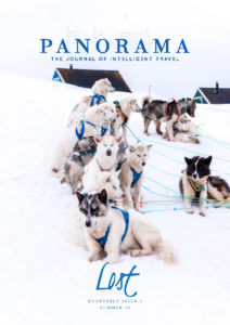 A team of sled dogs lined up in the snow in front of a snowy landscape, featured on the cover of panorama travel journal, summer '18 issue.
